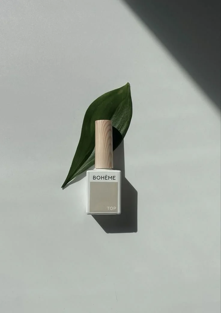 A nail polish bottle labeled 'BOHÈME TOP' with a green leaf and shadow on a white surface.