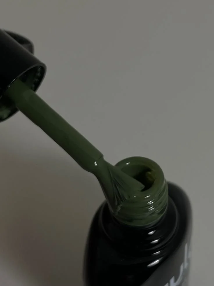 Close-up of dark green nail polish being poured from a bottle with a brush applicator.