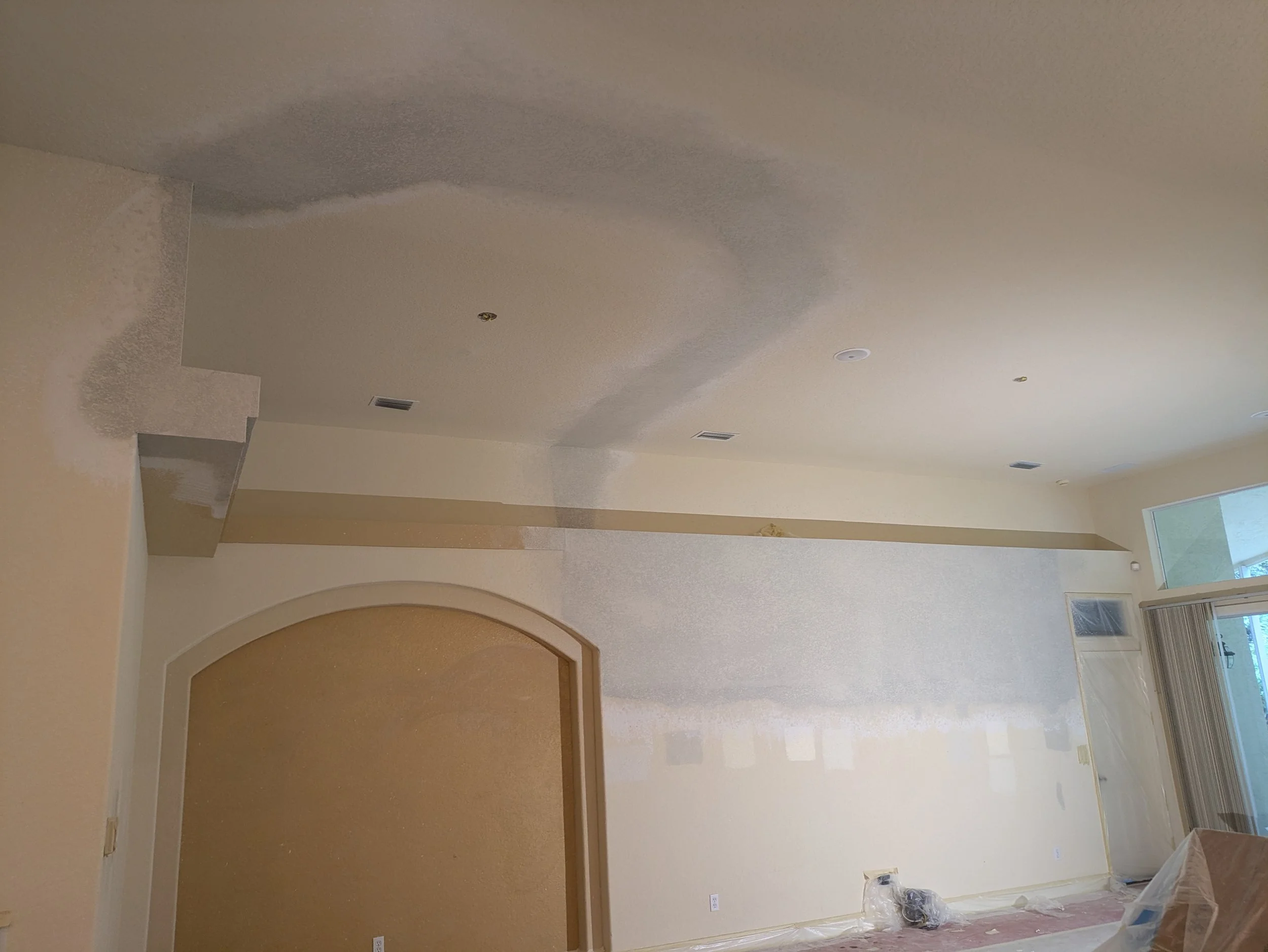 Living room with partially painted or primed walls and ceiling, construction materials on the floor, and a sliding glass door with vertical blinds.