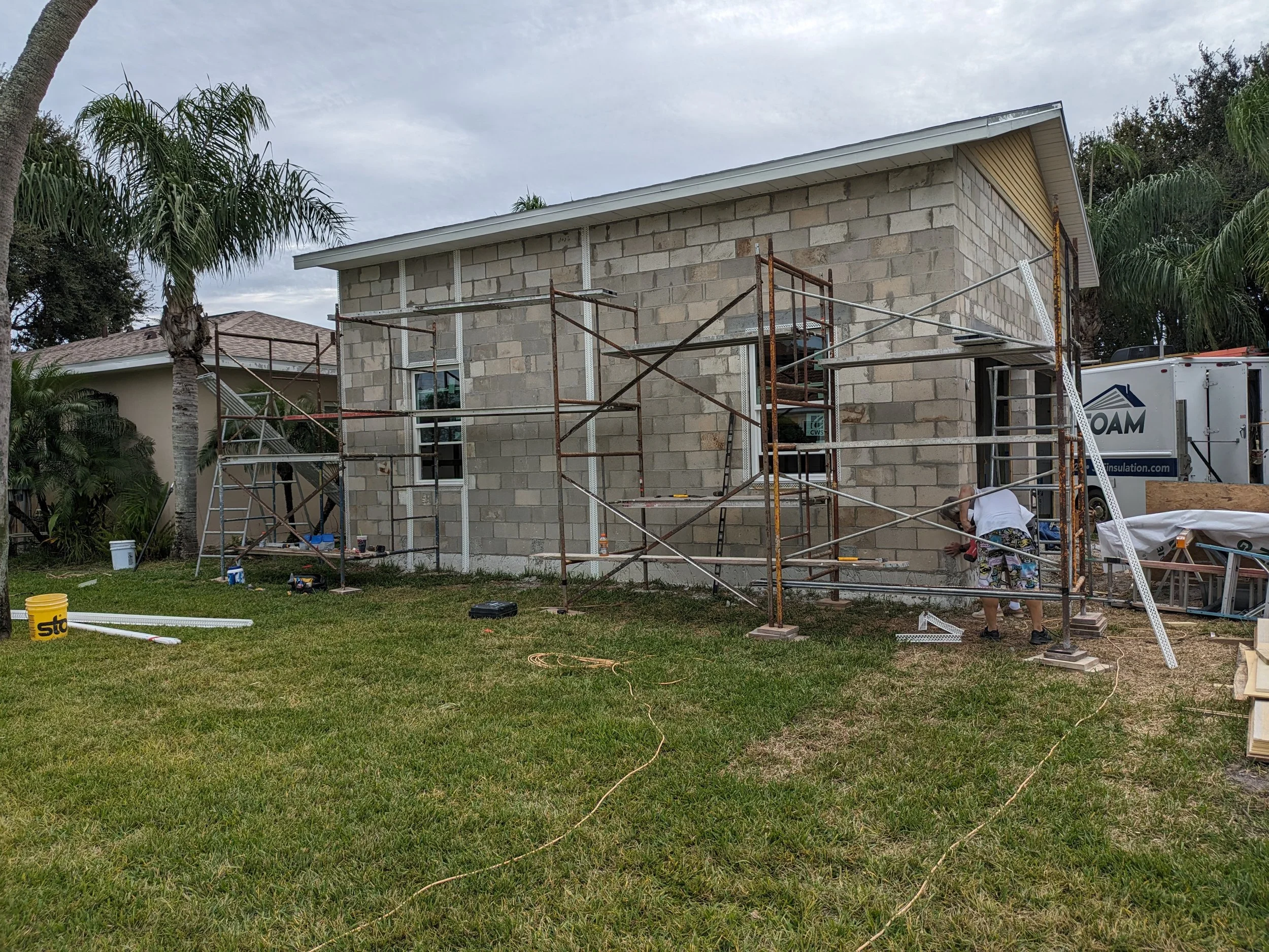Construction worker working on the exterior of a house with scaffolding, brick walls, and construction tools and materials on the lawn.