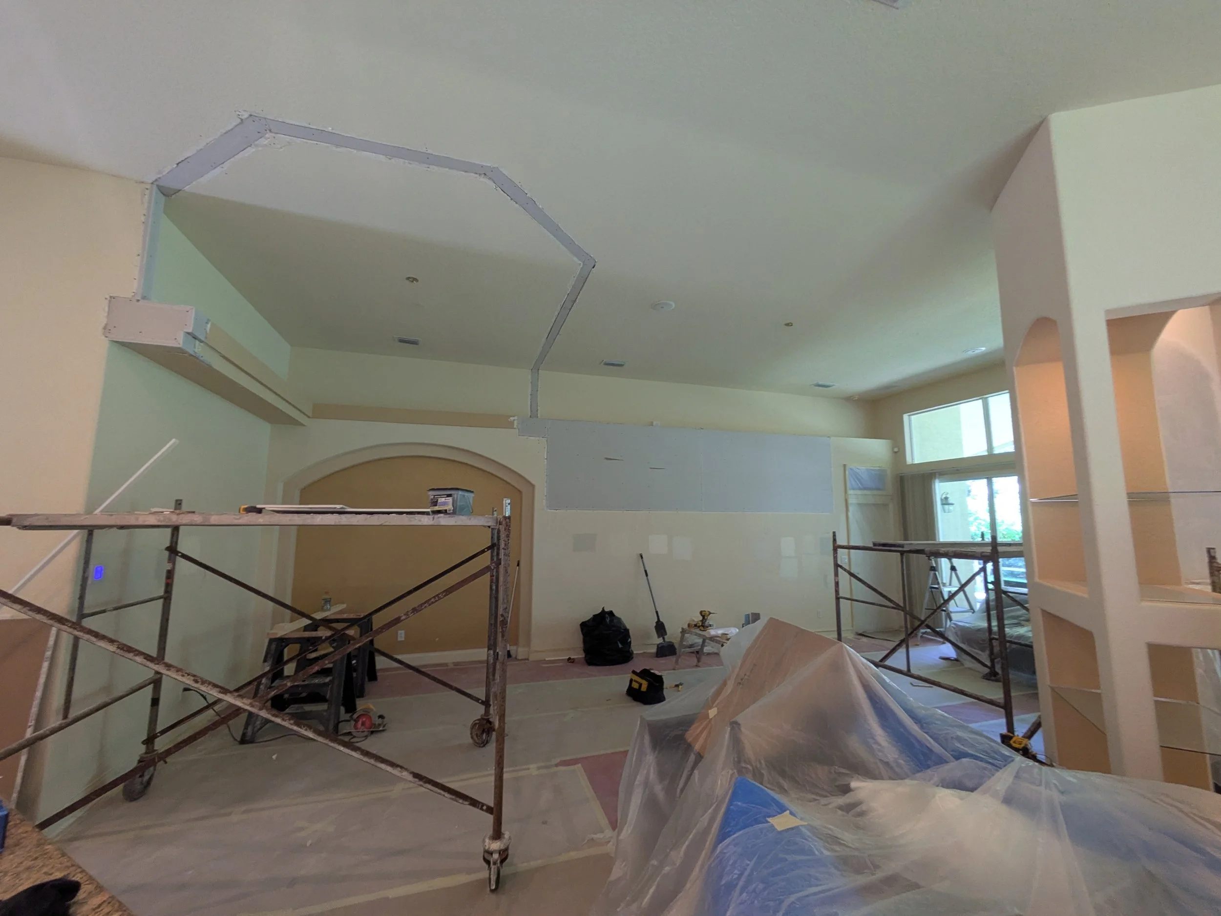 Interior of a house under renovation with scaffolding, construction tools, and partially painted walls.