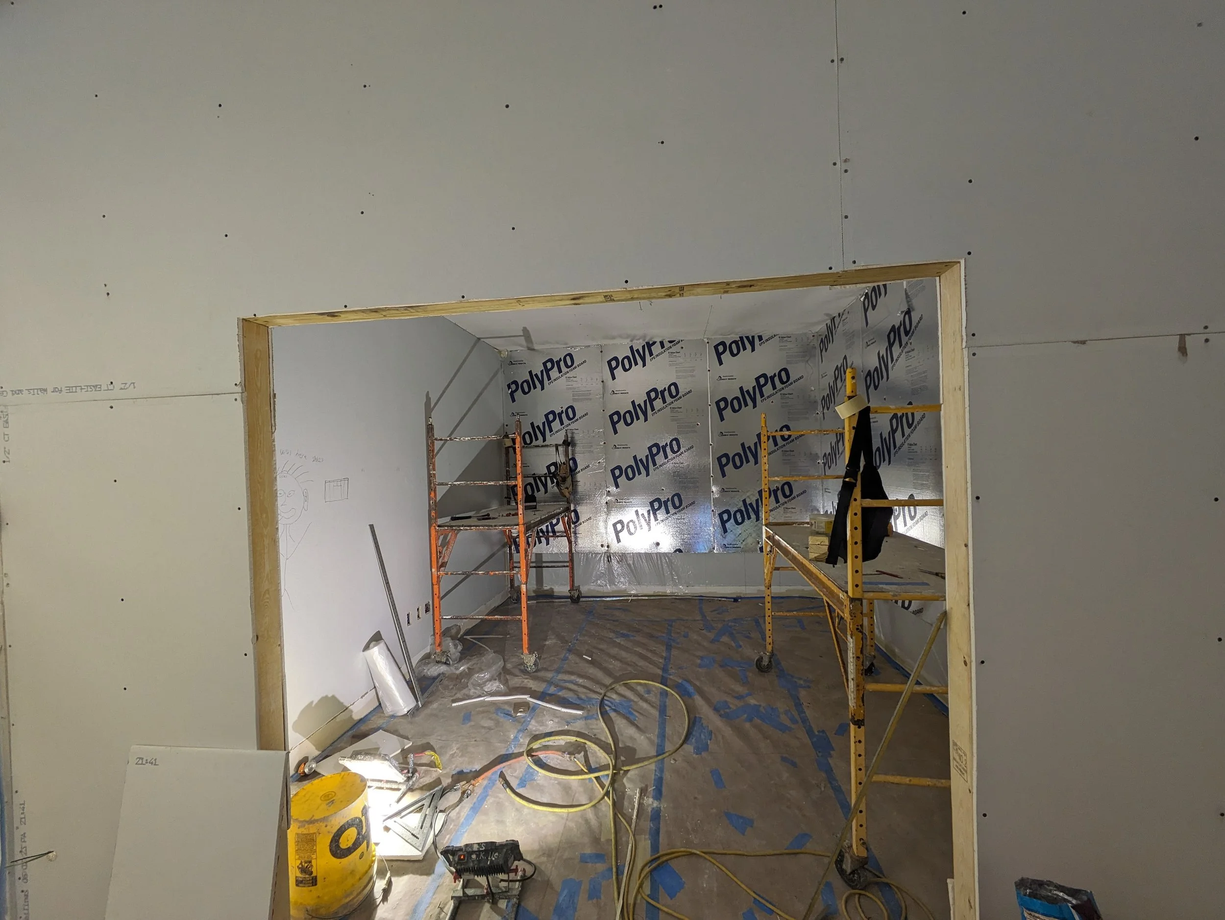Construction site showing an unfinished doorway with drywall and scaffolding inside, construction tools and materials on the floor.