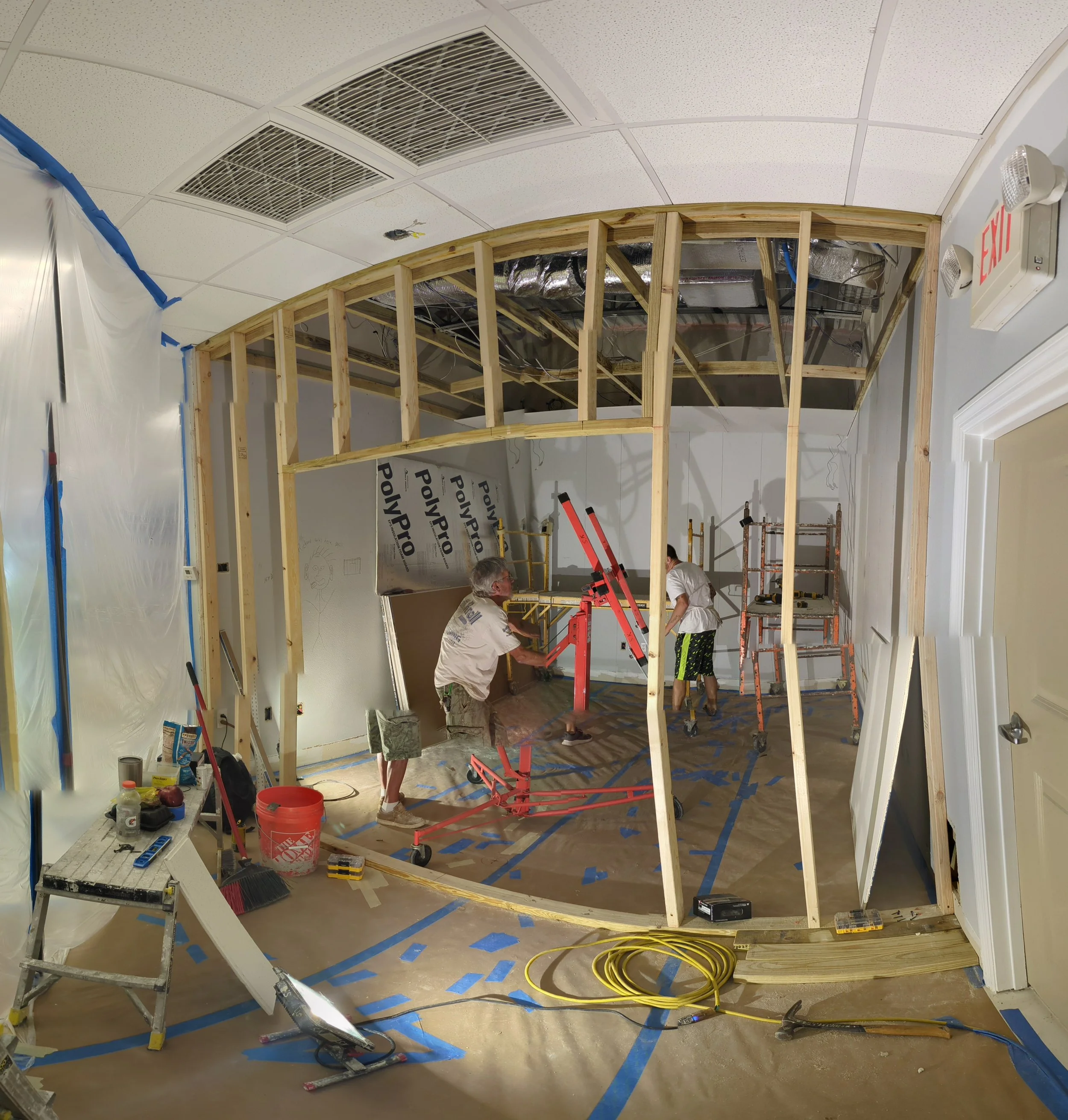 Construction workers building a wooden wall inside an office space with scaffolding, tools, and construction materials around.