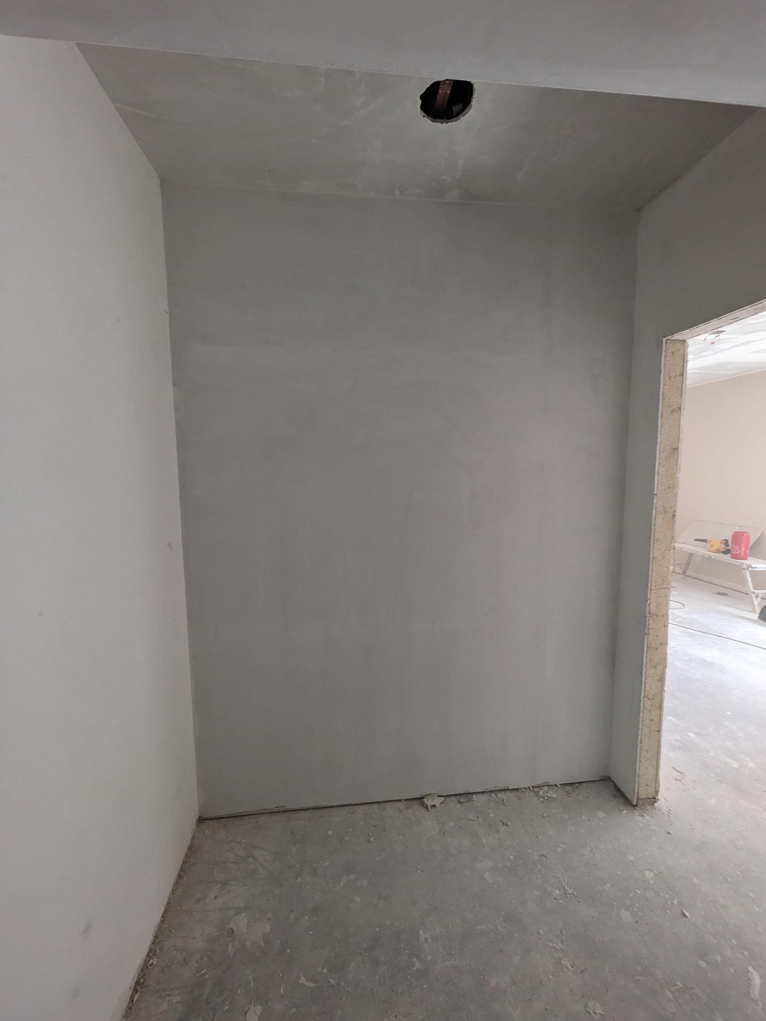 Interior of a room under construction with drywall installed, an open hole in the ceiling, and unfinished flooring.