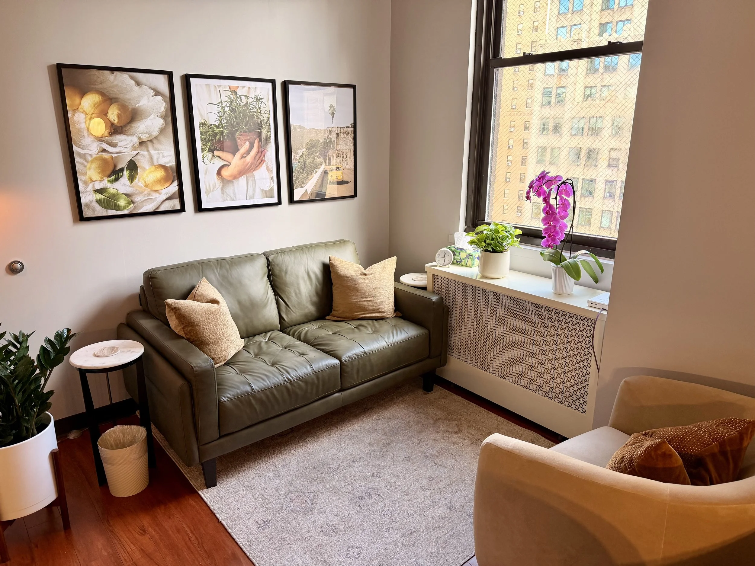 A cozy therapy office room with a green sofa, beige armchair, and orchid, showing a New York City therapy practice focused on evidence-based therapy for adults, families and couples.