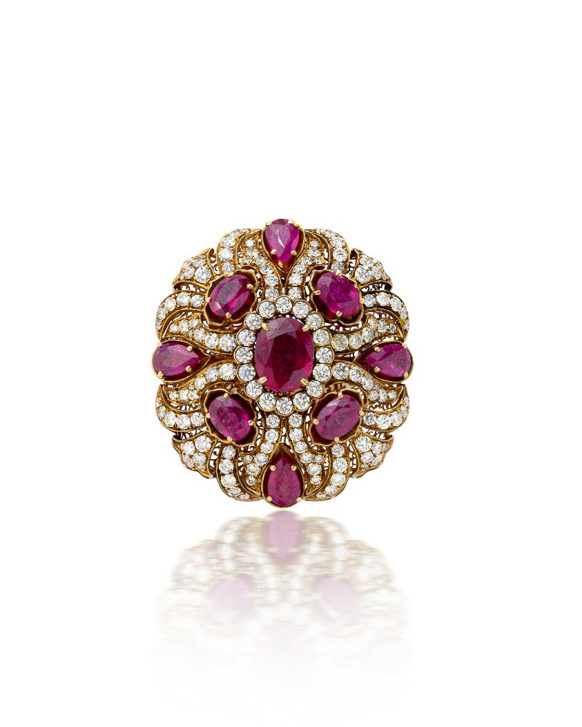 An ornate gold ring with multiple large pink gemstones and numerous small diamonds set around them, creating a floral or sunburst design.
