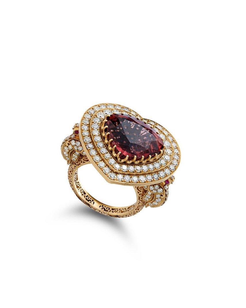 Gold ring with a large oval red gemstone surrounded by small diamonds, ornate design, and additional small red gemstones on the band.