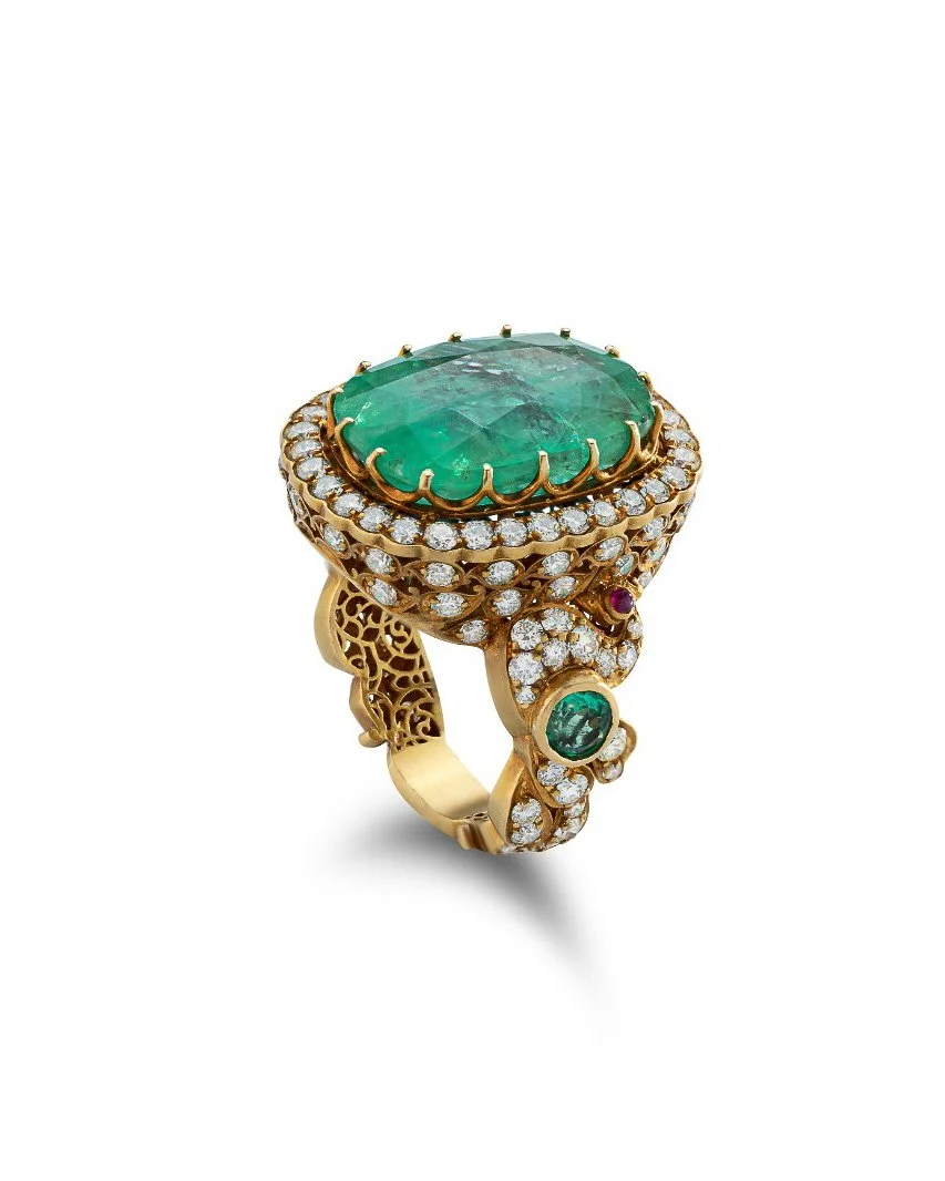 Gold ring with a large oval green gemstone surrounded by small diamonds, and additional diamonds and smaller green and red gemstones on the band.