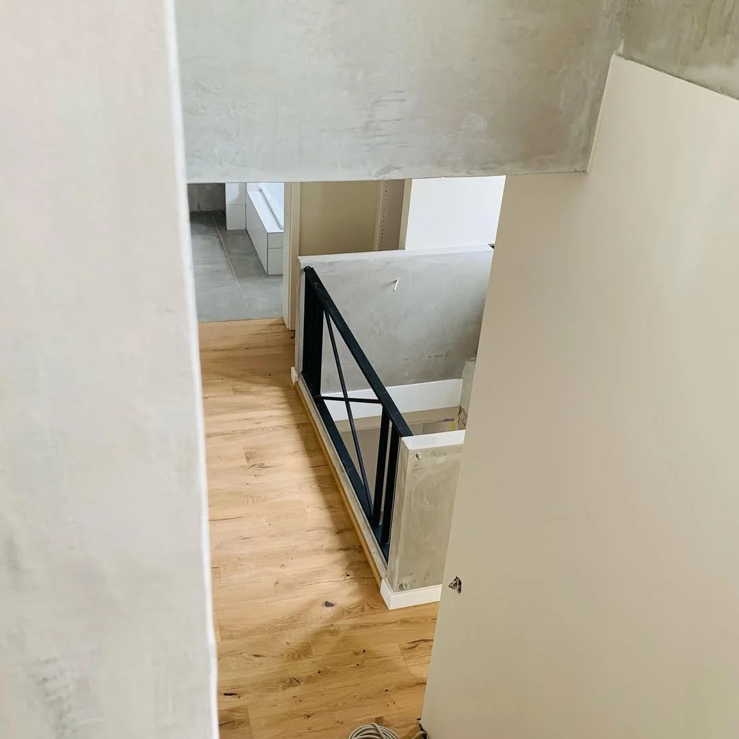 Innenansicht eines modernen Hauses mit einem Holzfußboden, einer schwarzen Metallbalustrade und Betonwänden.