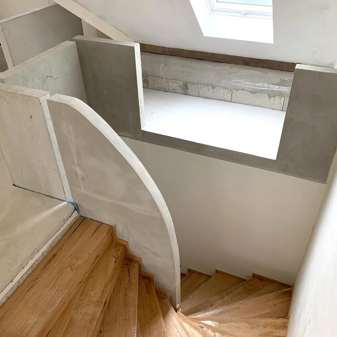 Innenaufnahme einer halb fertigen Holztreppe mit Betonwänden und einem Dachfenster.