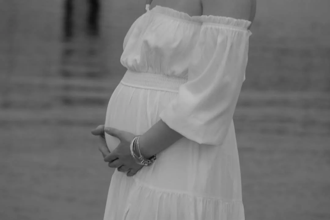 Black and white maternity portrait by Faith K Photography in Myrtle Beach SC, featuring expecting mother in flowing white dress holding her baby bump