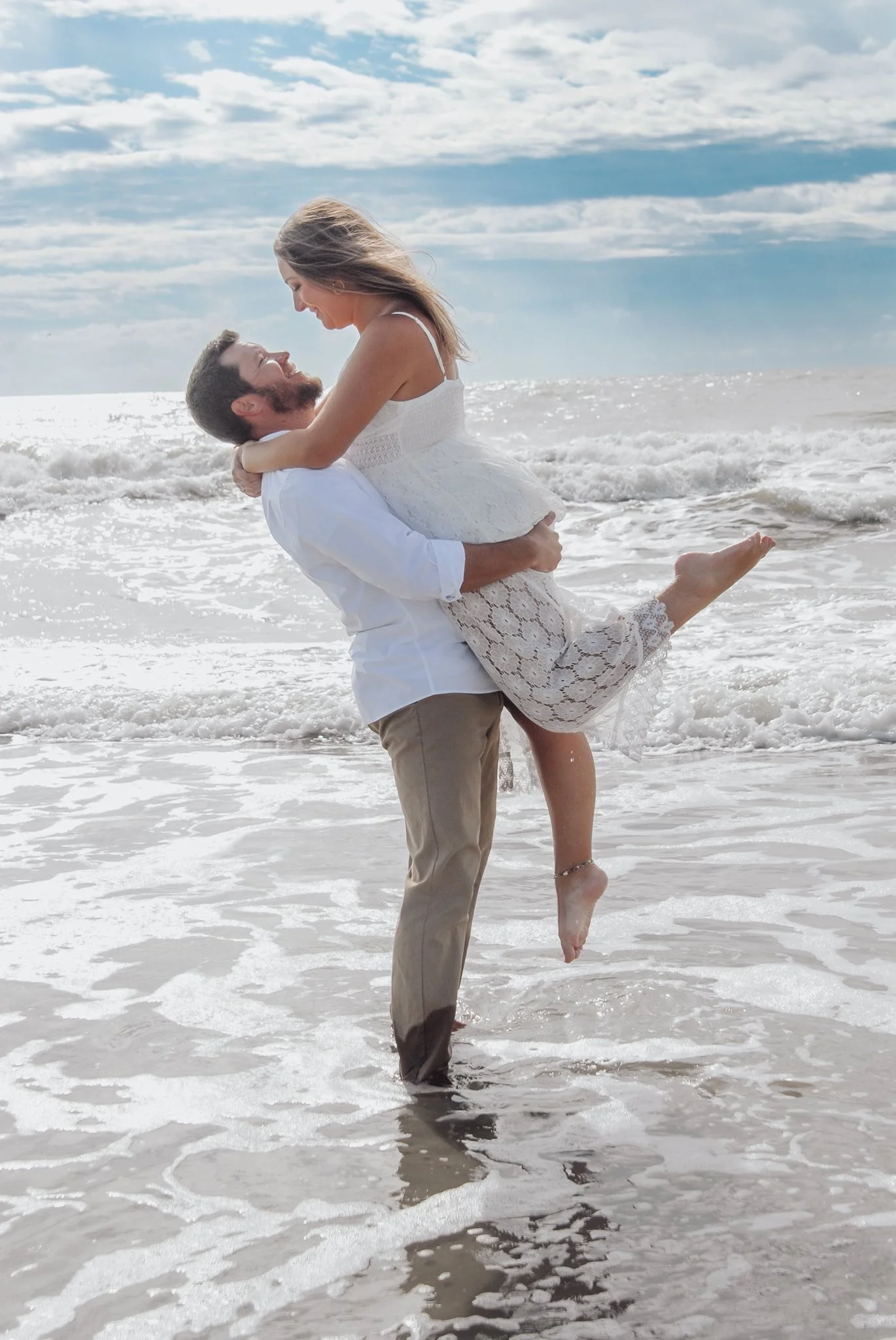 “Playful beach engagement photo by Faith K Photography in Myrtle Beach South Carolina featuring groom lifting bride in white lace dress near ocean waves.”