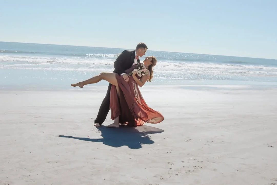 “Romantic beach couples portrait by Faith K Photography in Myrtle Beach, South Carolina featuring groom dipping bride in flowing burgundy dress by the ocean.”