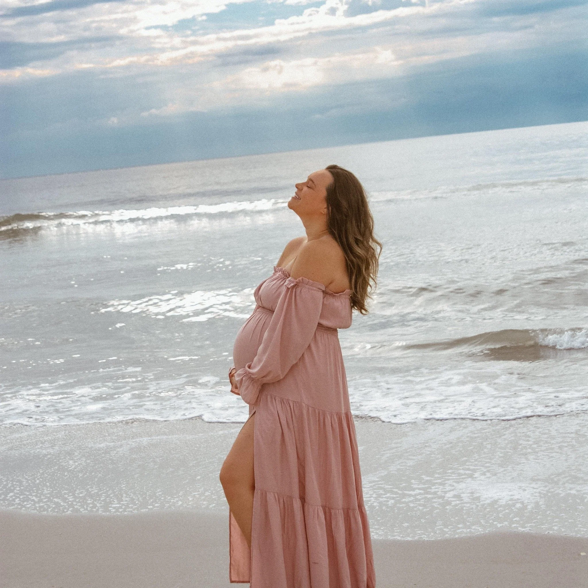 “Romantic coastal maternity session by Faith K Photography in Myrtle Beach South Carolina showing pregnant mother in flowing blush dress standing by ocean waves.”