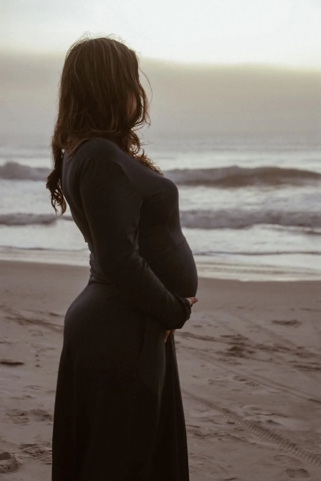Beach maternity portrait by Faith K Photography in Myrtle Beach, SC featuring expecting mother in fitted black gown holding her baby bump at sunset.