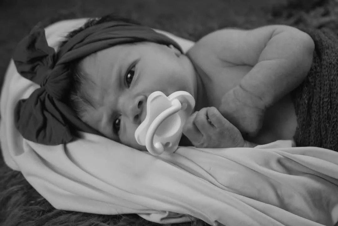 “Black and white newborn photography by Faith K Photography in Myrtle Beach, South Carolina featuring peaceful baby with pacifier lying on soft blanket.”
