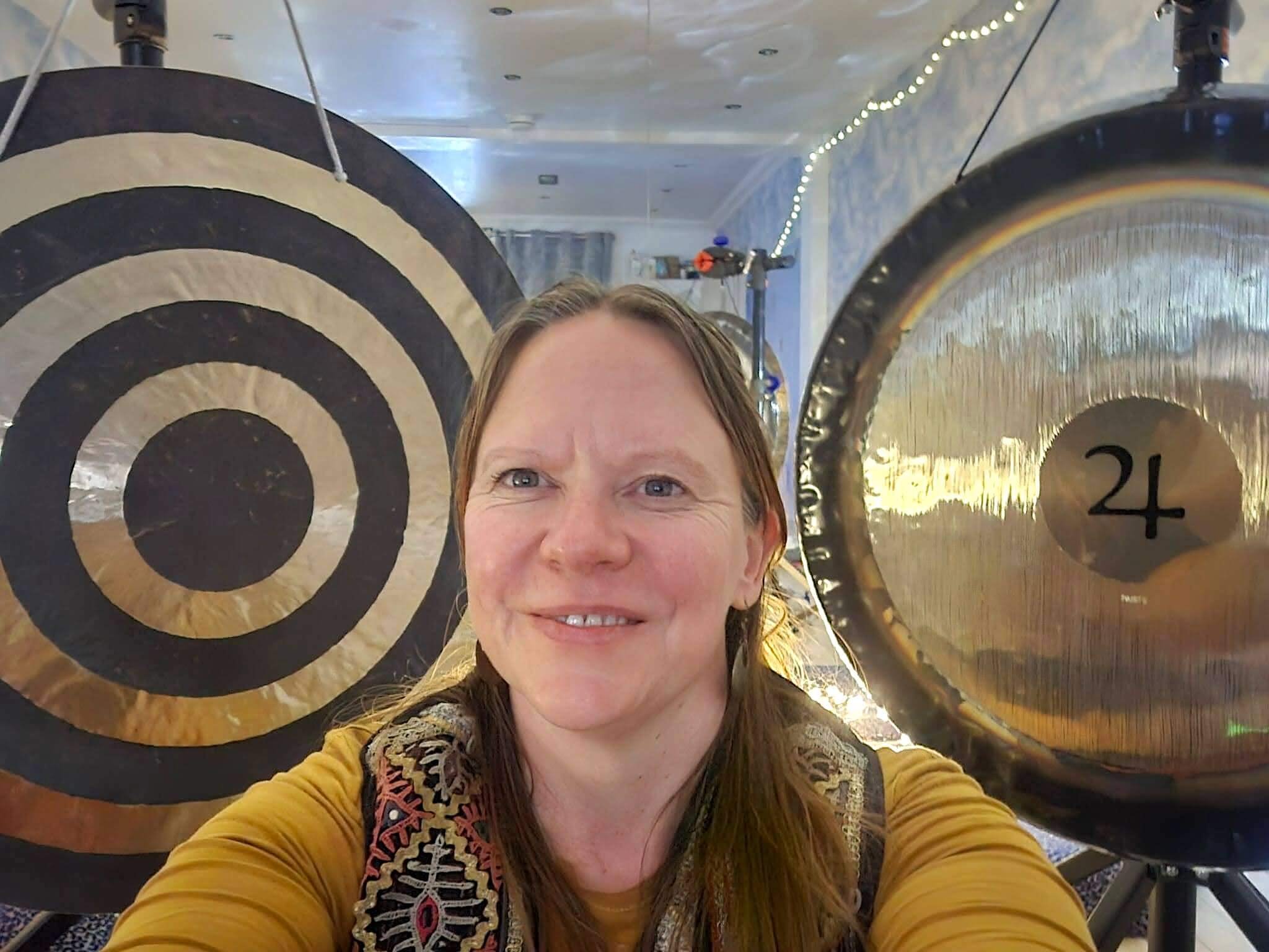 Woman taking a selfie in front of two large gongs, one with a target design and the other with the number 24.