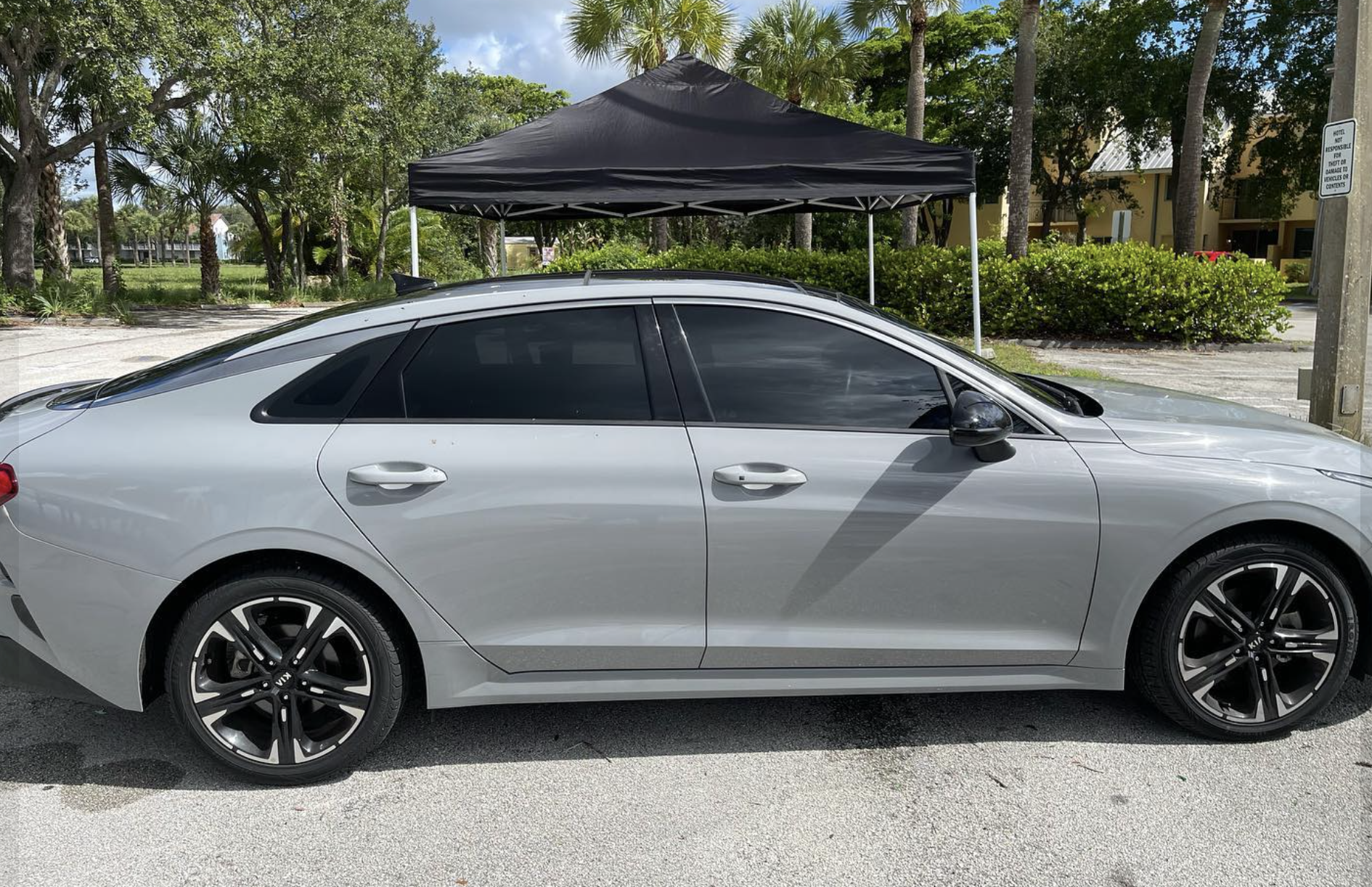 Silver sedan parked outdoors with a black canopy tent behind it, surrounded by trees and bushes.