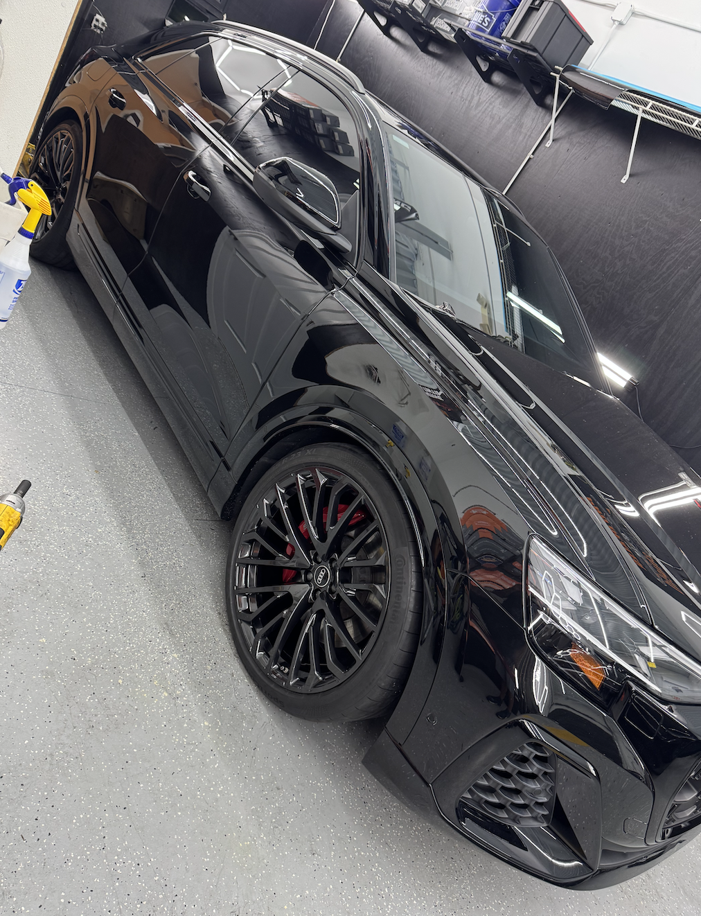 A black sports car with sporty black rims and red brake calipers parked inside a garage or workshop.