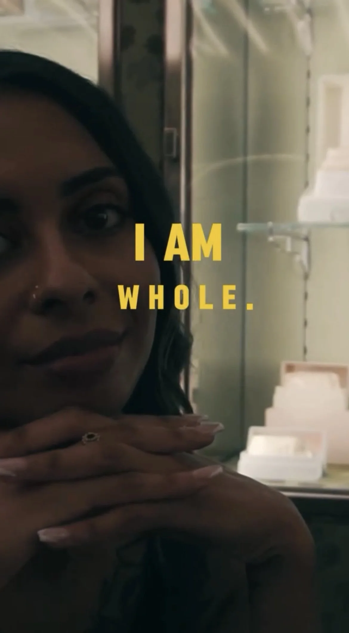 A woman with dark hair resting her chin on her hands. Overlay text reads "I AM WHOLE."