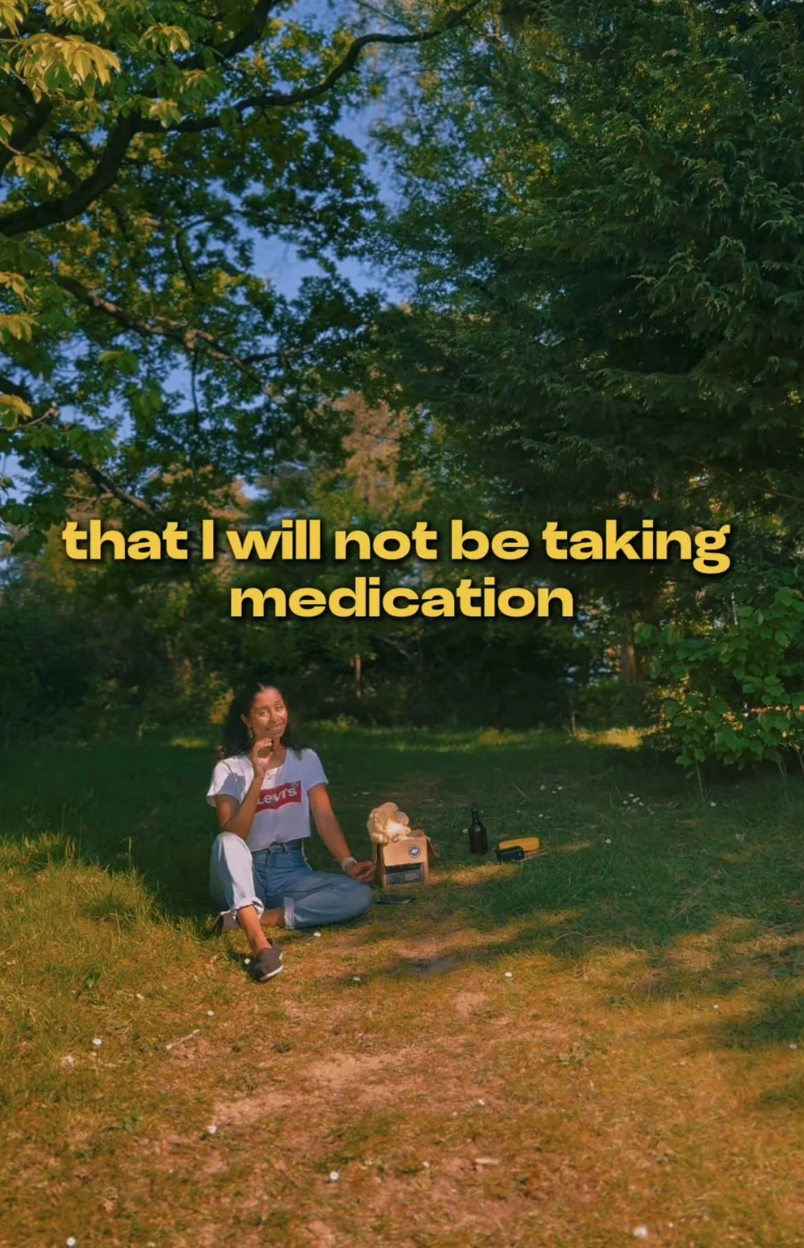 A woman sitting on the grass outdoors in a wooded area, holding a pill bottle, with a text overlay that reads 'that I will not be taking medication'.