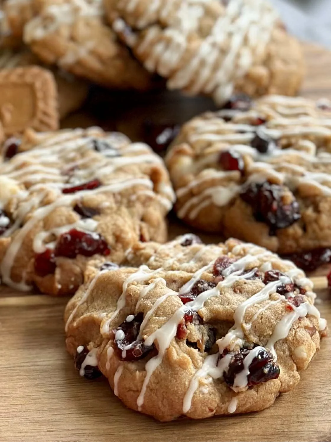 A close-up view of freshly baked cookies with berries, drizzled with white icing, arranged on a wooden surface.