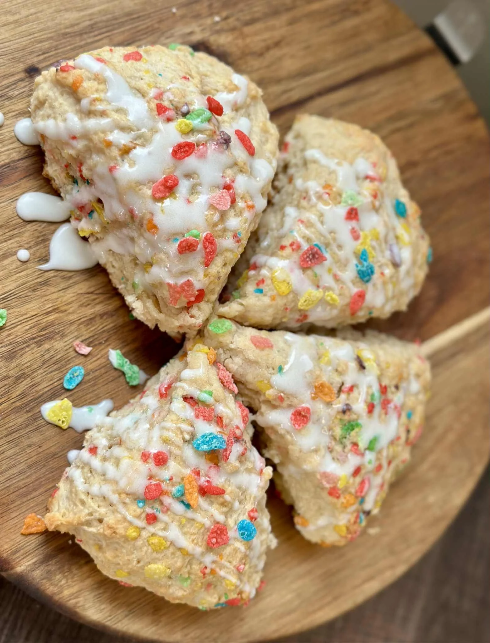 Three heart-shaped cookies with colorful sprinkles and white icing on a wooden plate.