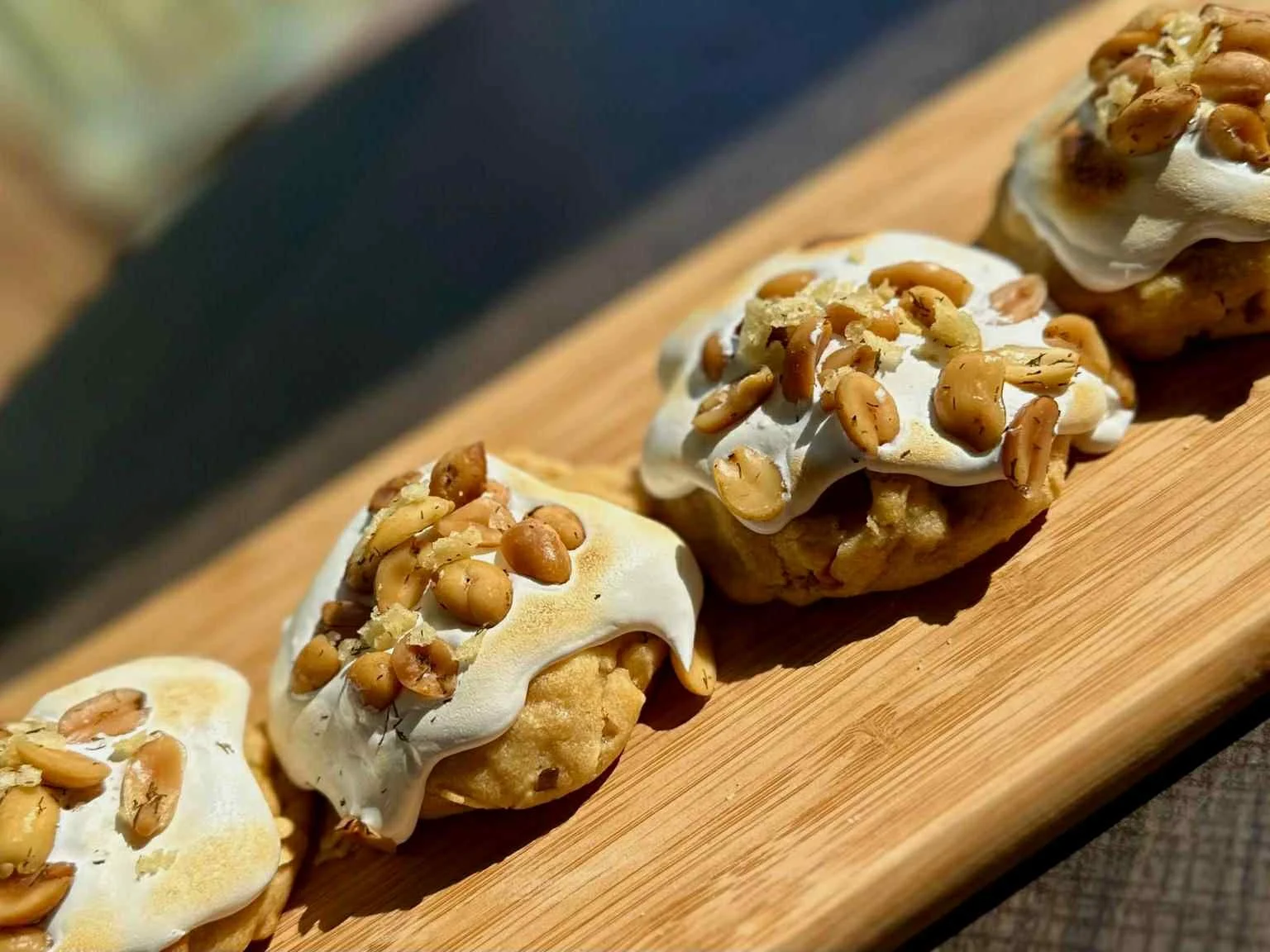 Three cookies topped with white frosting and chopped nuts on a wooden board.