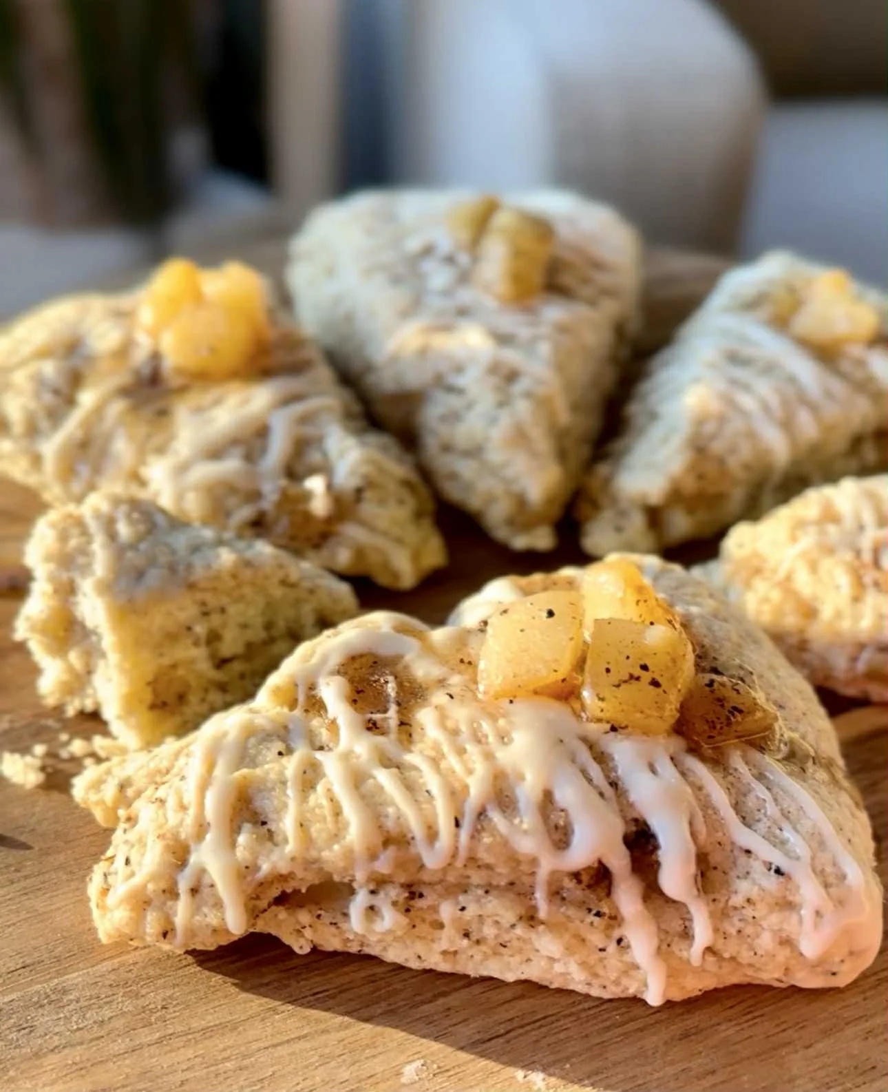 Close-up of multiple scones topped with icing and pineapple pieces on a wooden cutting board.