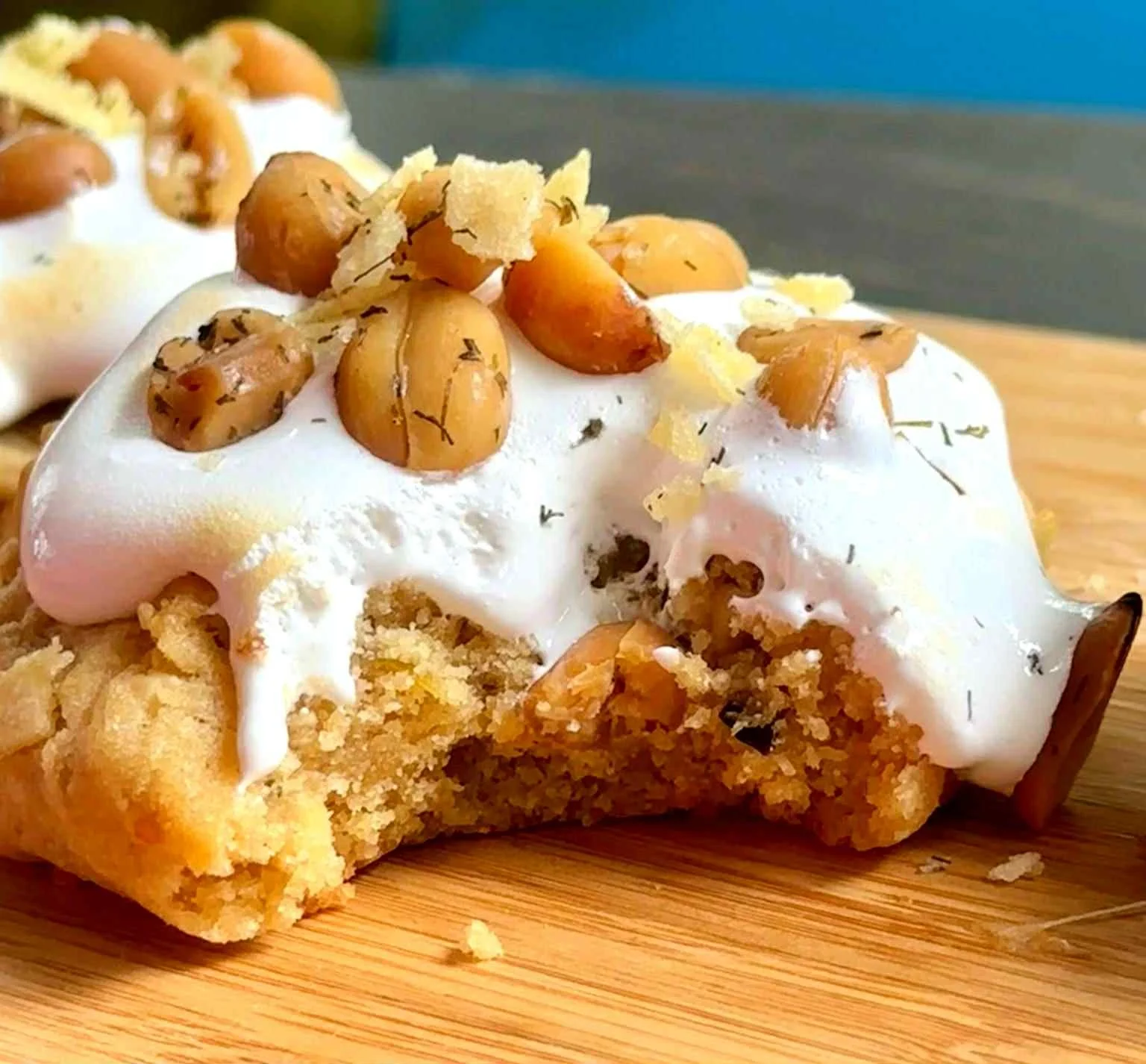 A slice of pie with a crumbly crust, topped with whipped cream, roasted pine nuts, and sprigs of herbs on a wooden surface.