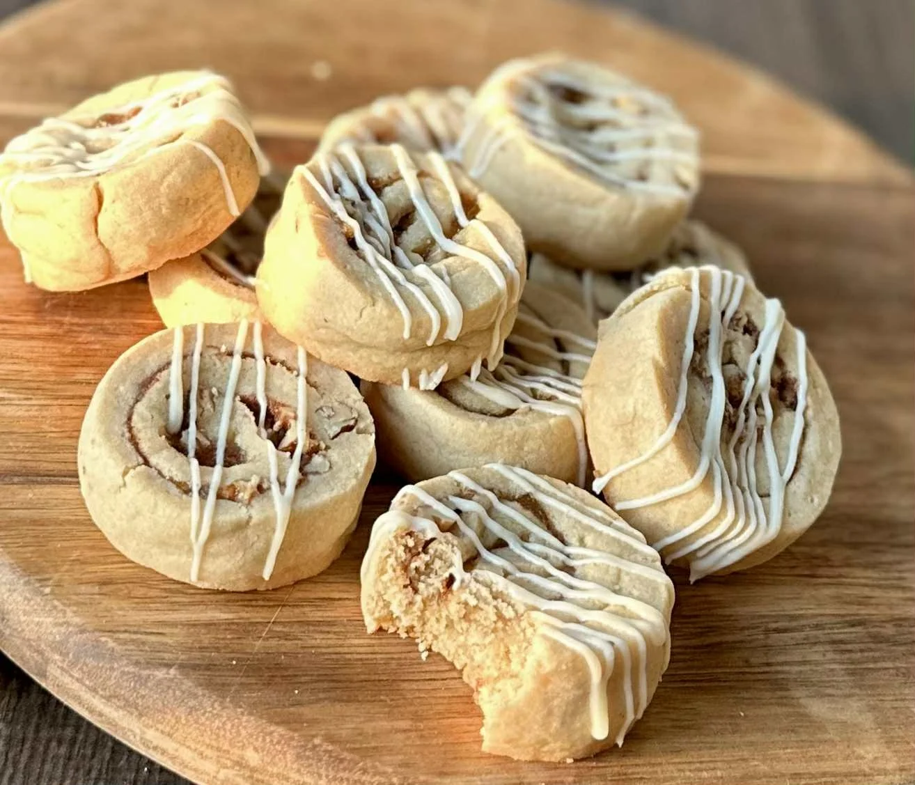 Group of cinnamon rolls drizzled with white icing on a wooden platter.
