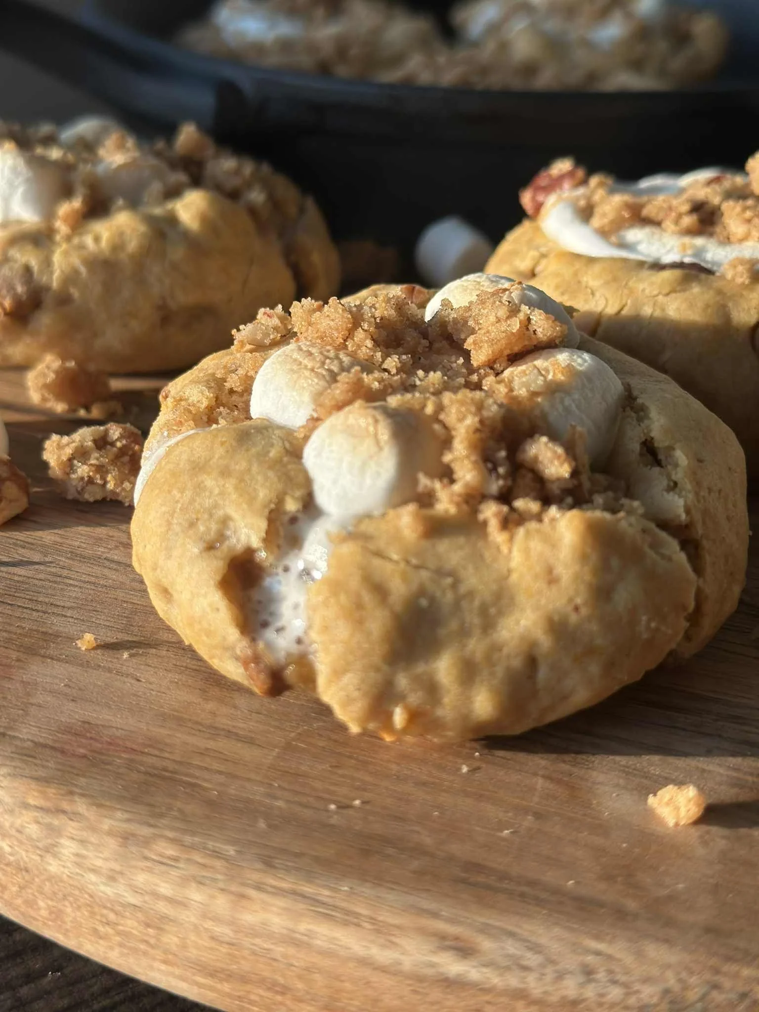 Close-up of a s'mores dessert on a wooden board, topped with marshmallows and crumbled graham crackers.
