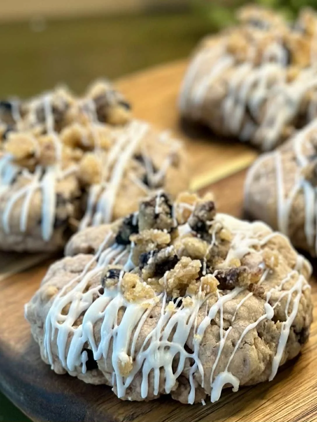 Close-up of cookies with white icing and crumbly topping on a wooden tray.