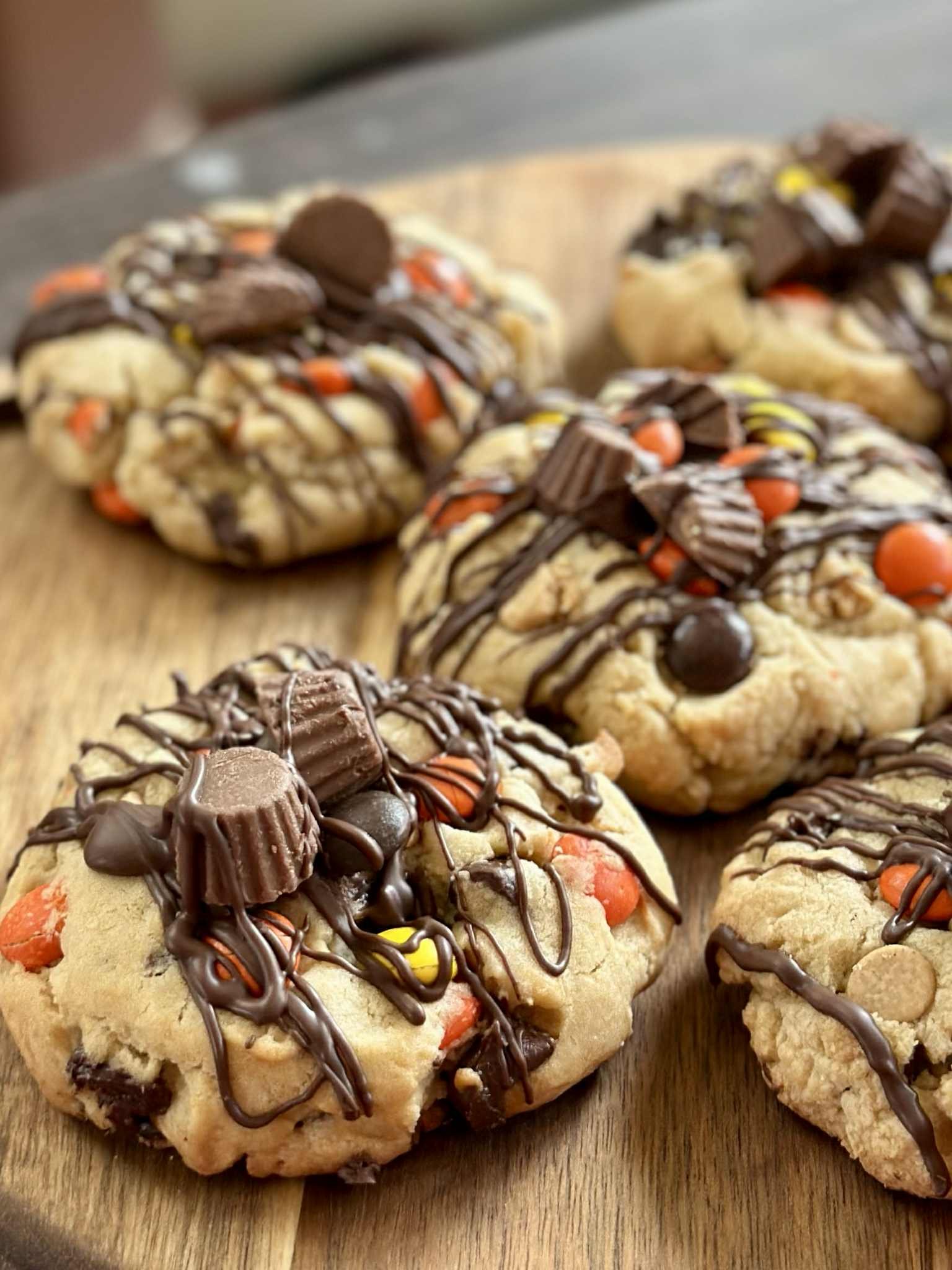 Close-up of five decorated cookies with chocolate drizzle, candies, and chocolate pieces on a wooden plate.