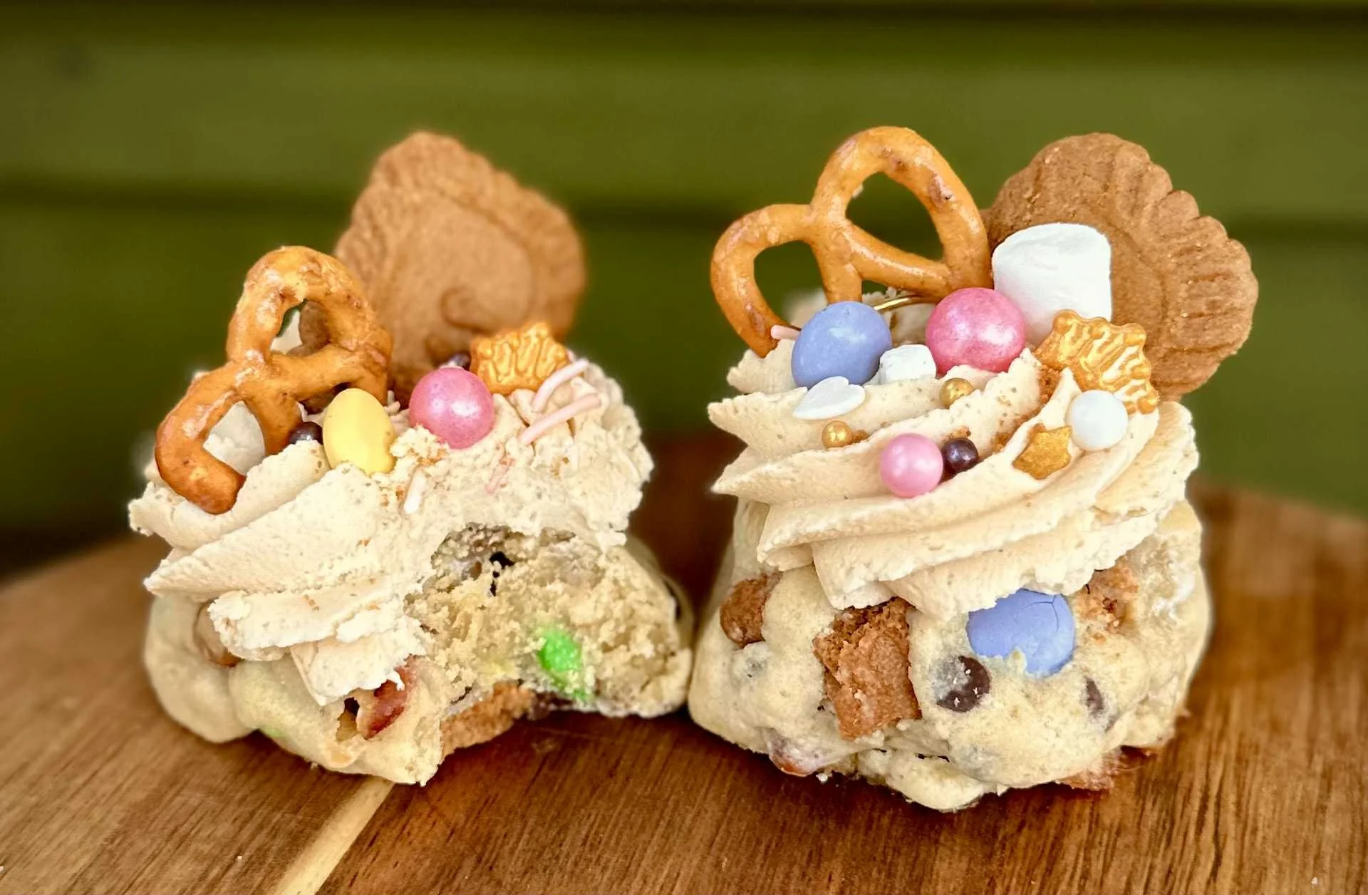 Decorated cookies with frosting, pretzels, colorful candies, sprinkles, and edible gold accents on a wooden surface with a green background.