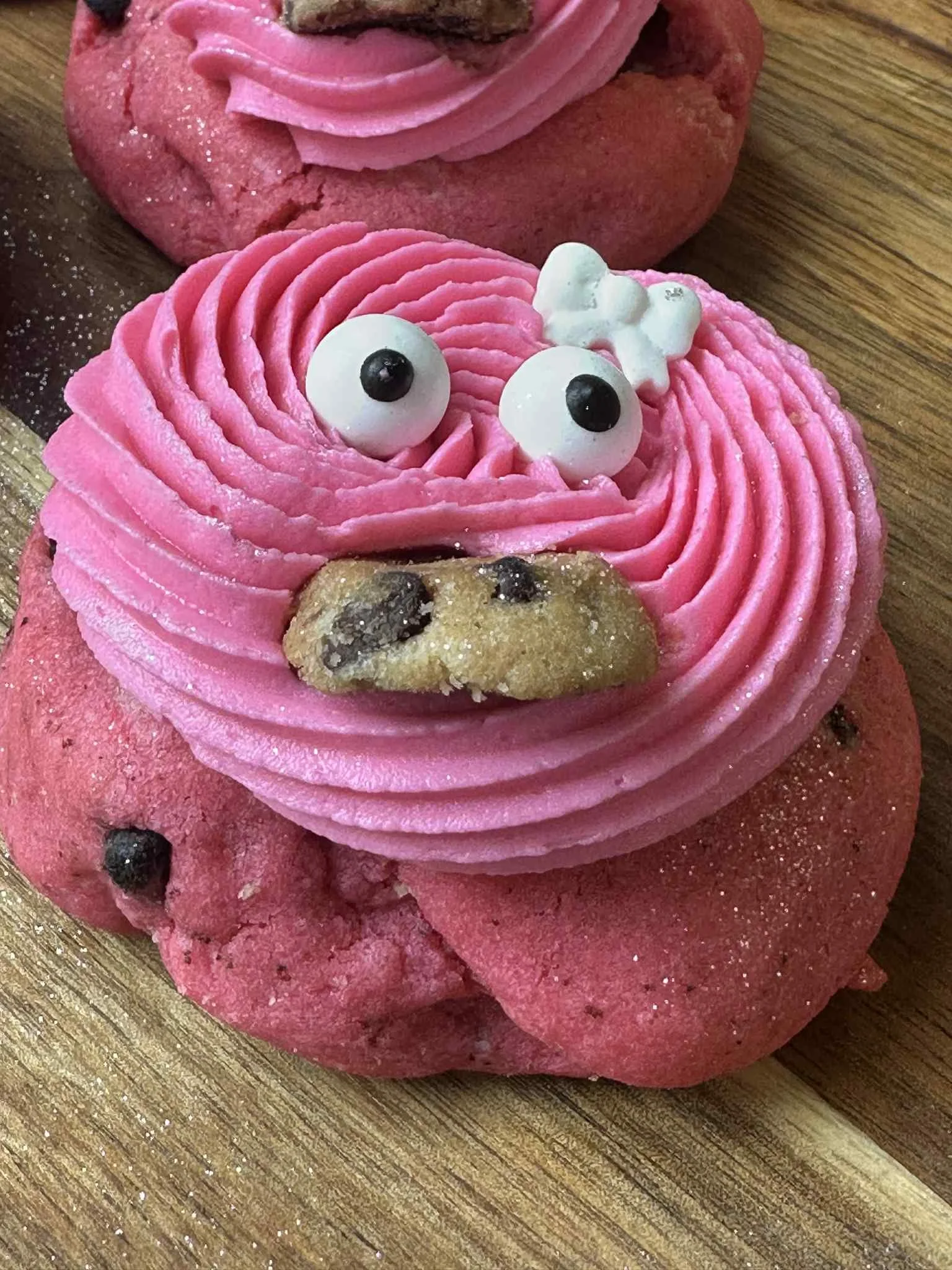 Cookie decorated to look like a cute puppy, with pink frosting piped in swirls, blue candy eyes, a cookie nose, and small white candy accents on a wooden surface.