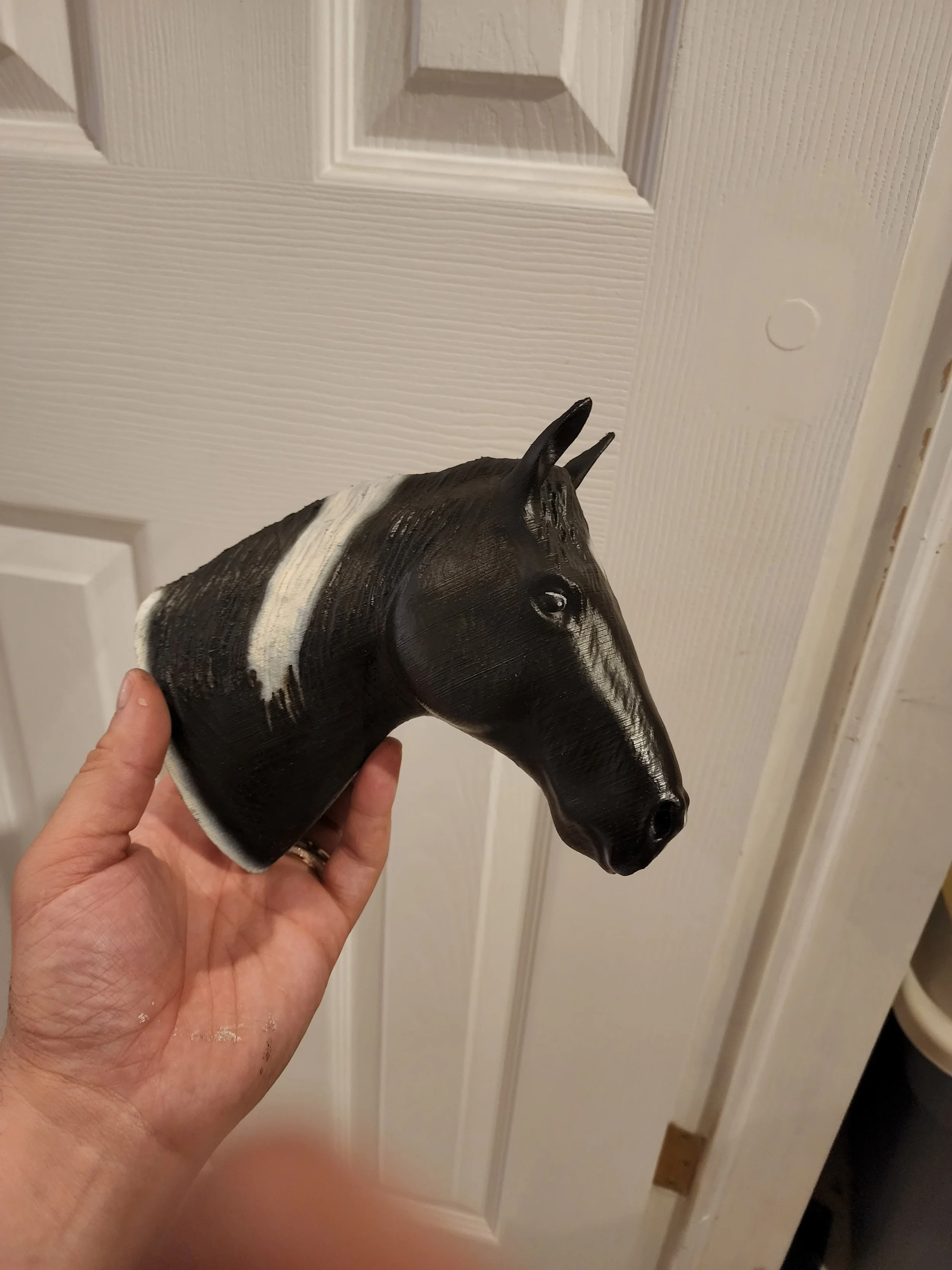 A person holding a black and white horse head sculpture in front of a white door.