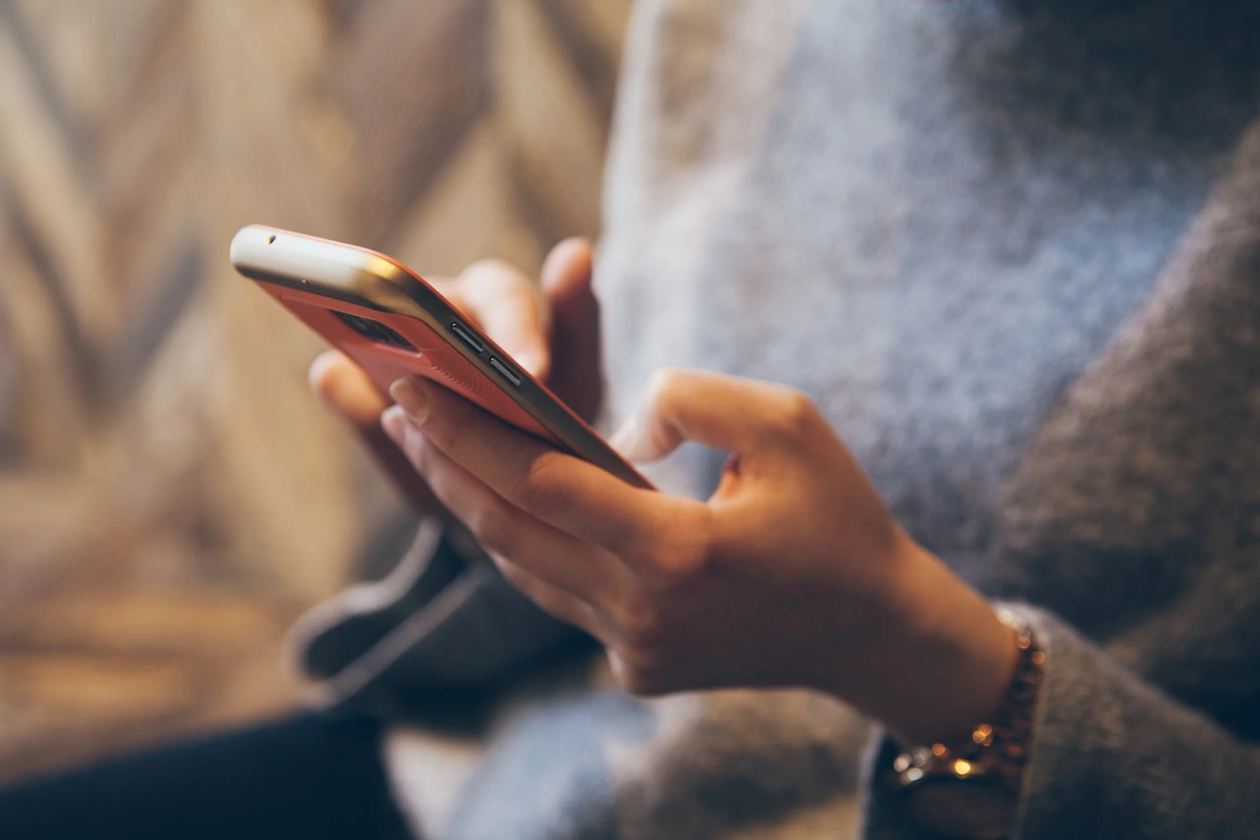 Close-up of a person holding and using a smartphone with one hand, wearing a bracelet and a gray sweater.