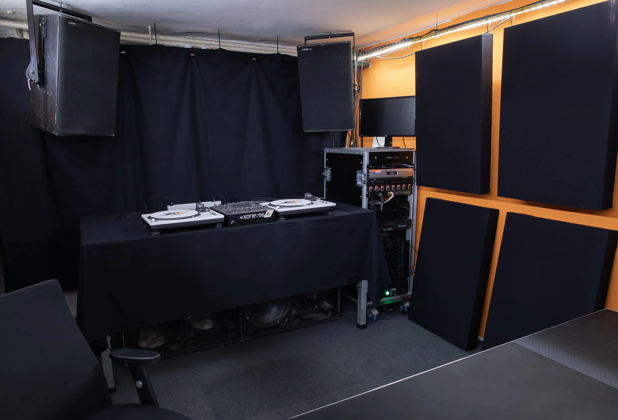 DJ setup with turntables, mixer, monitors, and soundproofing panels in a studio or event space.