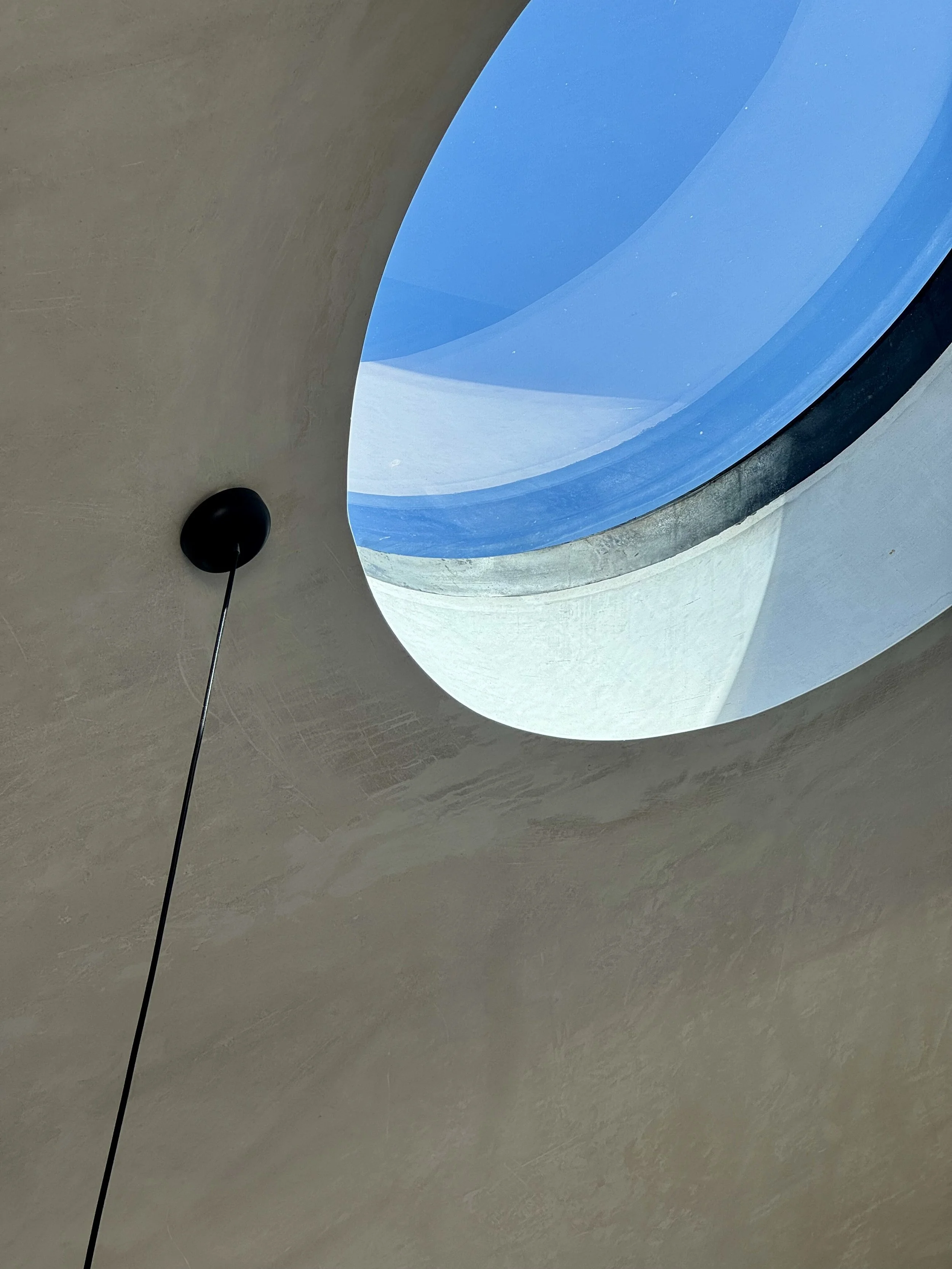 Looking up at a ceiling with a circular skylight showing a blue sky and part of a building outside.