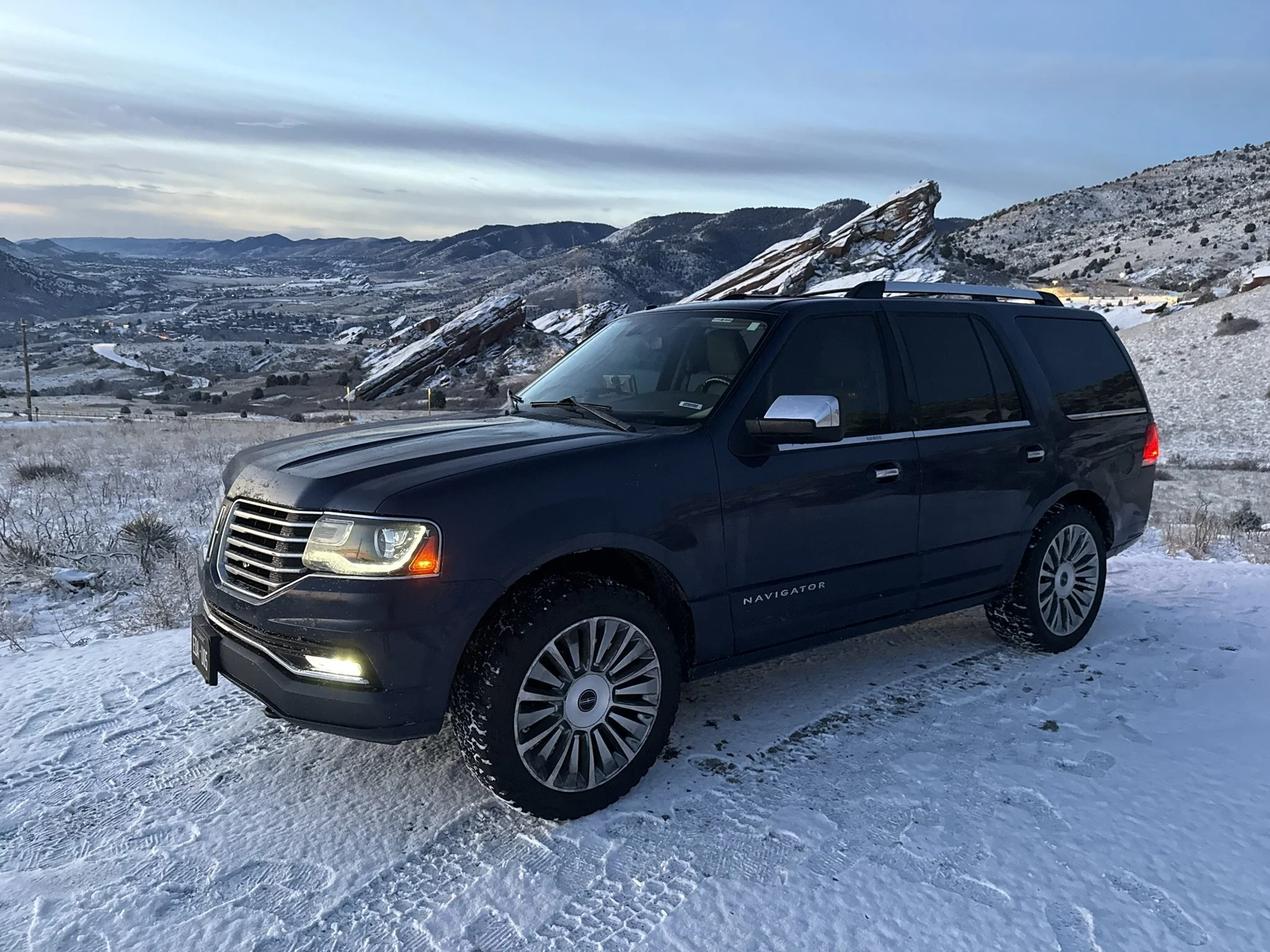 Blue 2015 Lincoln Navigator SUV rental parked on snowy ground with a mountainous winter landscape in Colorado