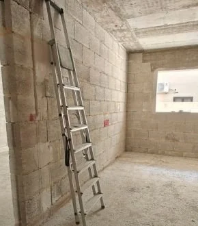Ladder leaning against unfinished concrete wall in a room under construction.