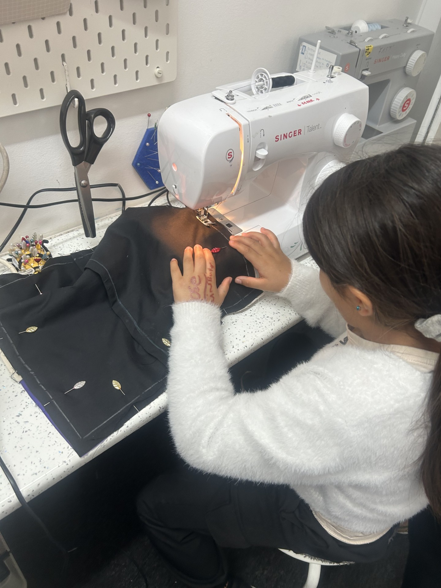 A young girl sewing fabric on a sewing machine in a workshop or classroom setting.