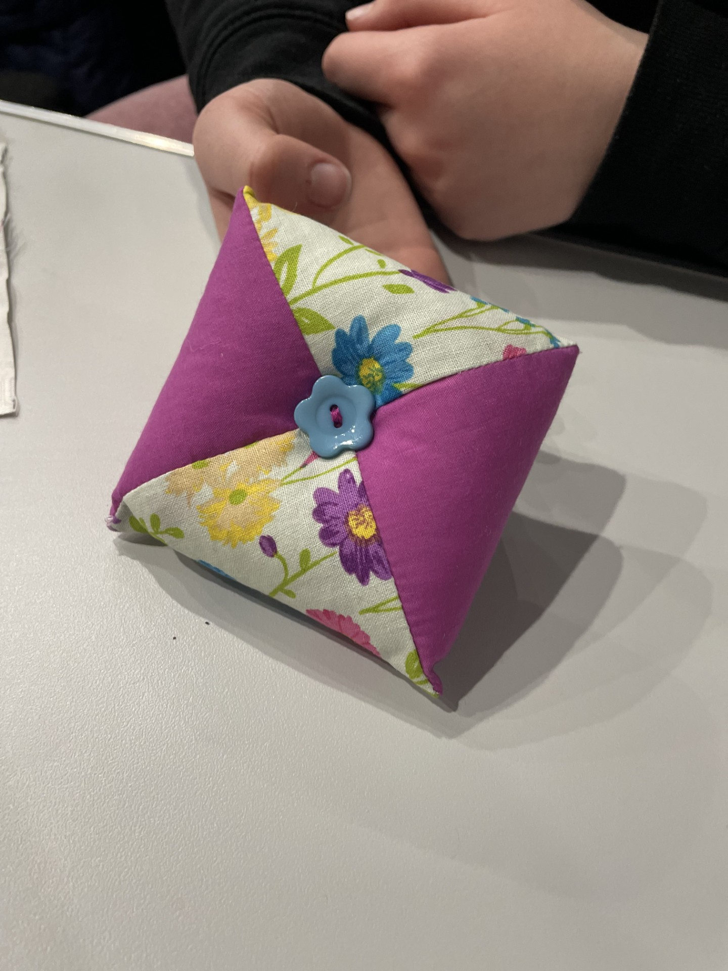 A fabric pyramid-shaped package with pink and floral patterned fabric, decorated with a small blue flower-shaped button.