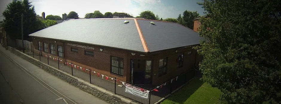 A brick building with a gray sloped roof and windows, set beside a sidewalk and street, decorated with red, white, and blue bunting, and surrounded by trees.