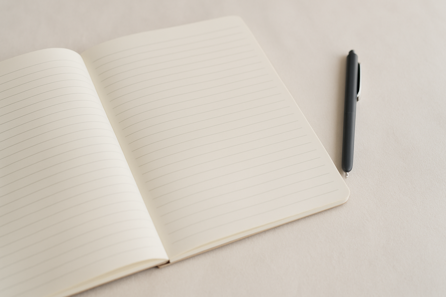 Open notebook with lined pages and a black pen on a white surface.