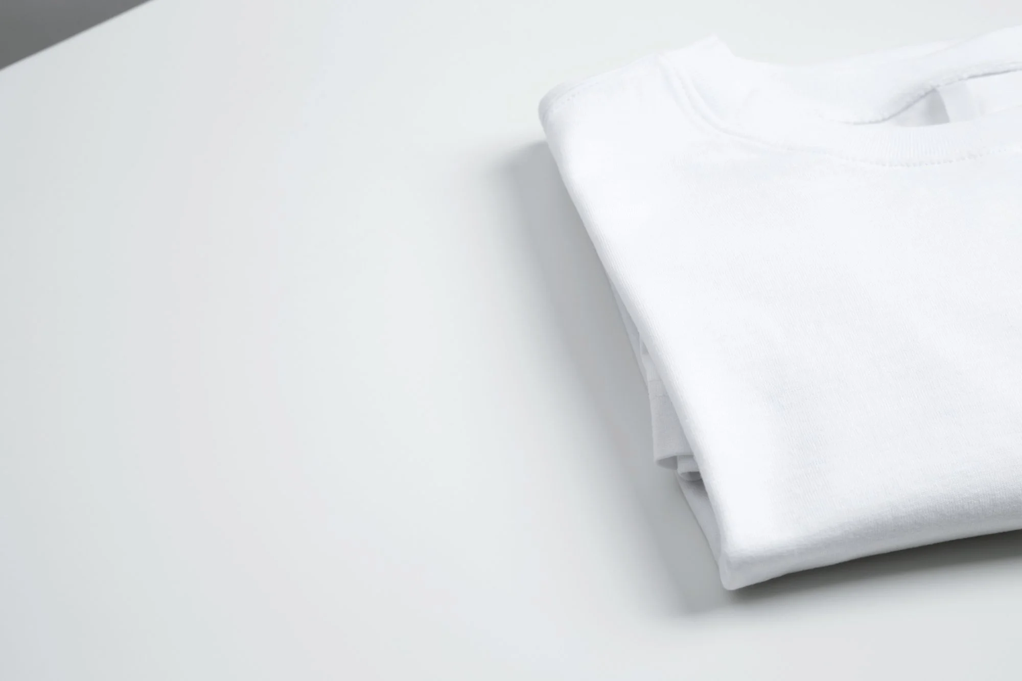 Folded white t-shirt on a white surface.