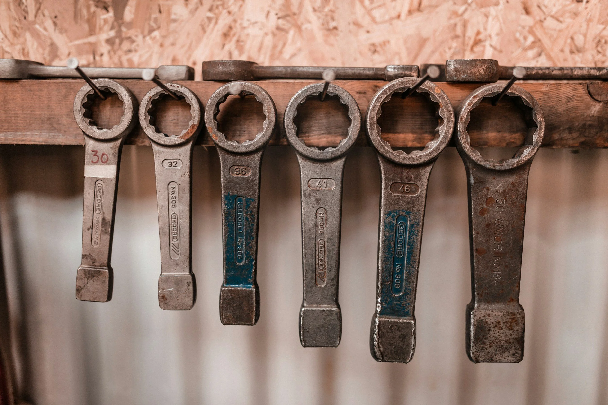 A row of metal wrenches hanging on a wooden pegboard, arranged from smallest to largest.