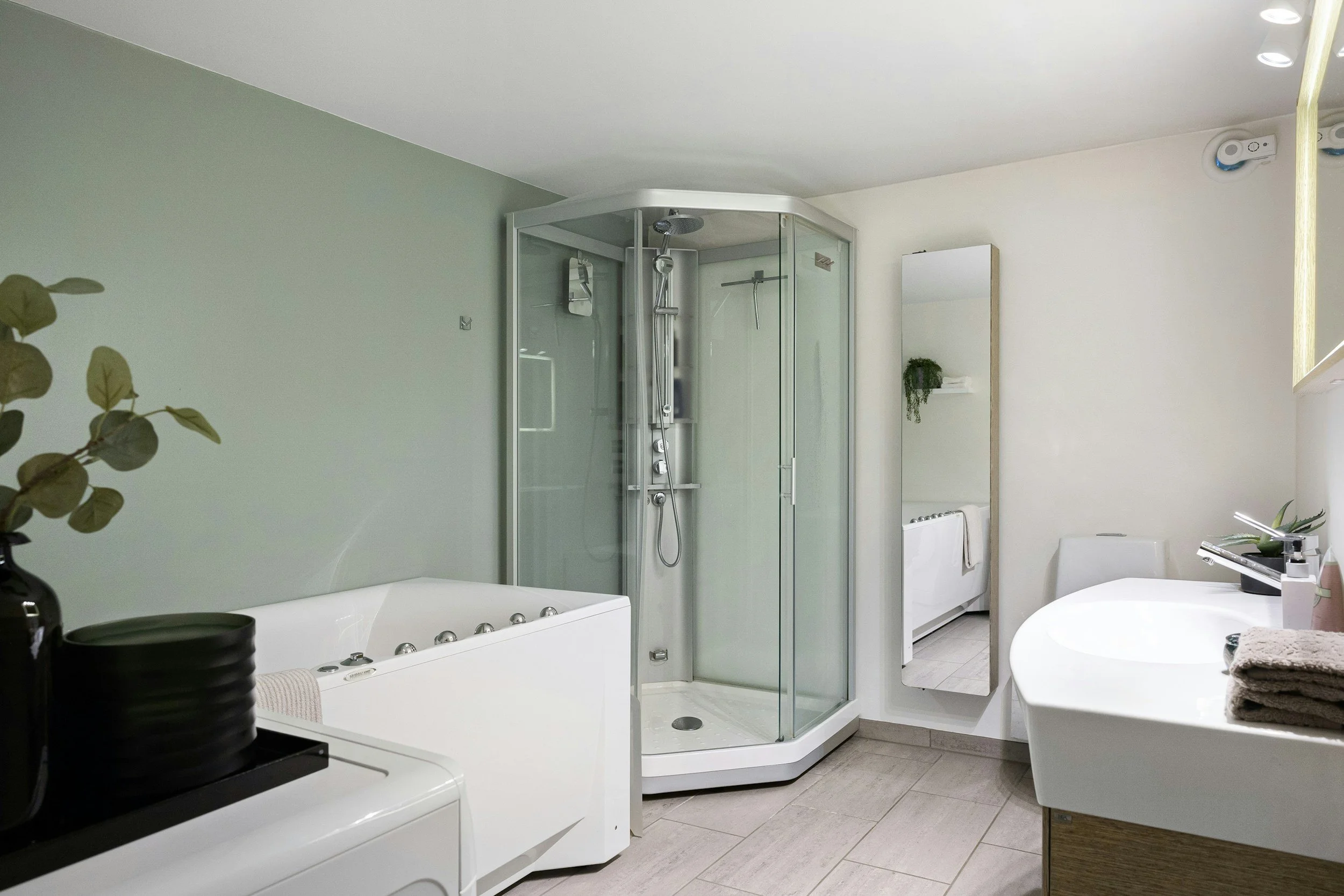 Modern bathroom with a corner shower enclosure, a white bathtub with jets, a sink with a faucet, and various plants and towels for decoration.