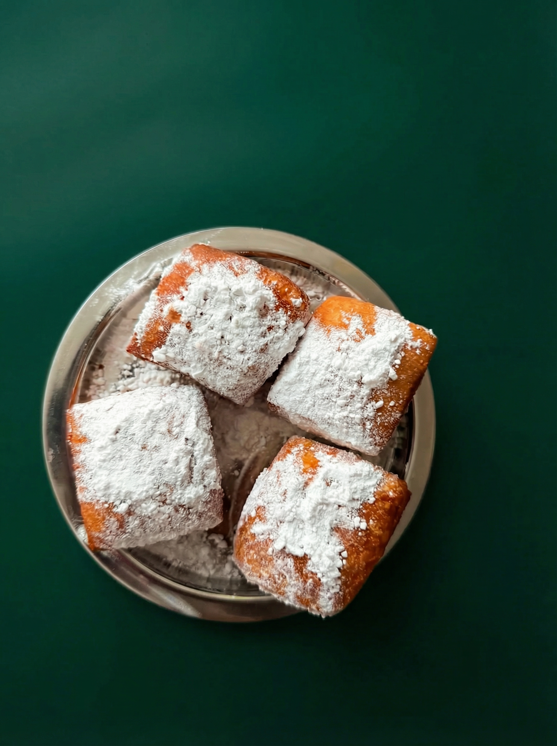 Powdered sugar dusted beignets in a green box with the Beignet Beignet logo.